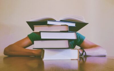 student hiding behind a pile of books